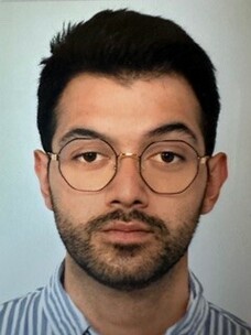 Lorenzo Gomez mit dunklem Haar, Brille und ernstem Blick vor grauem Hintergrund.